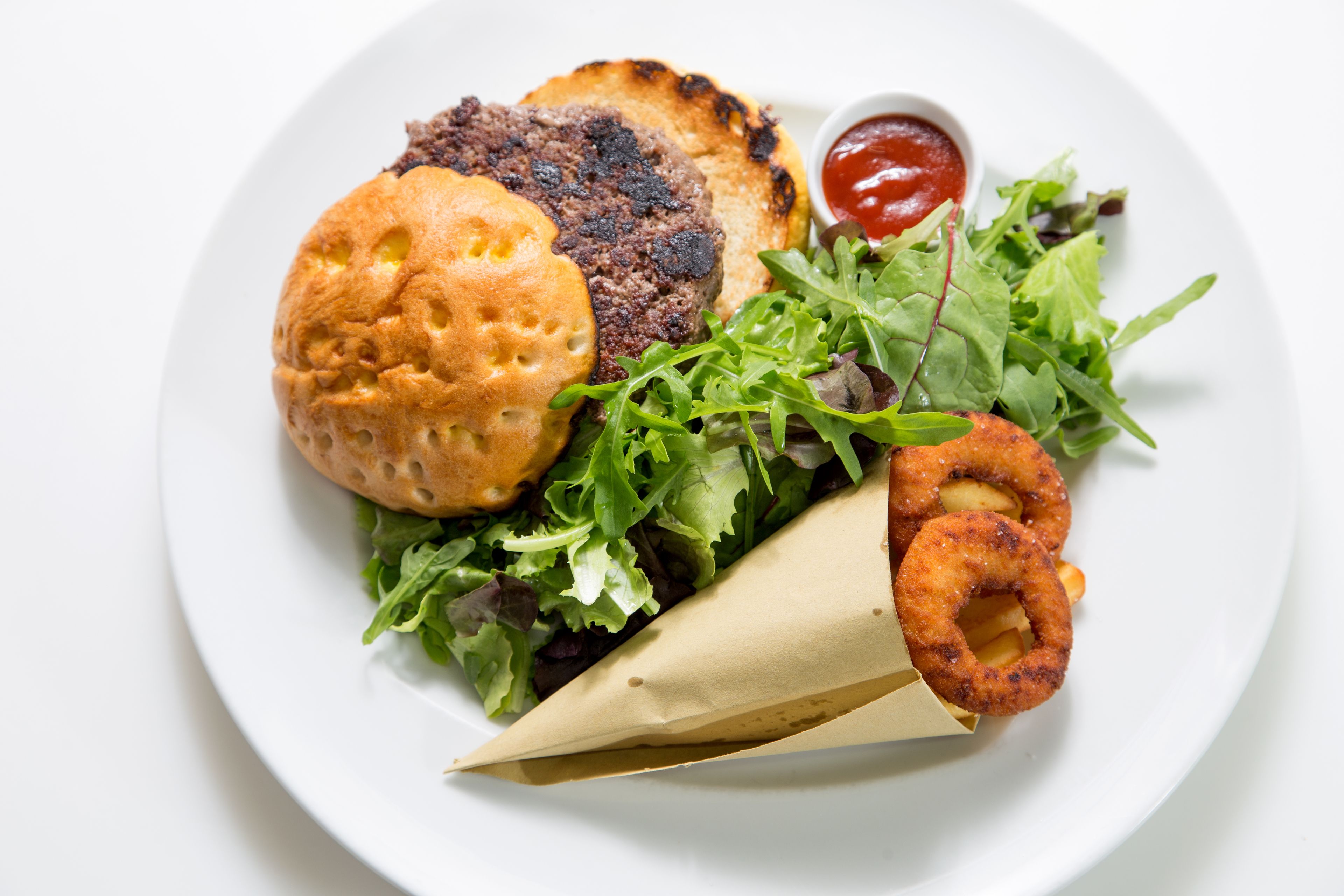 Un plato con una hamburguesa, ensalada, aros de cebolla y kétchup.