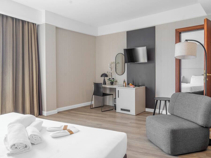 A hotel room with a bed, a desk, a chair, a TV, and a lamp.