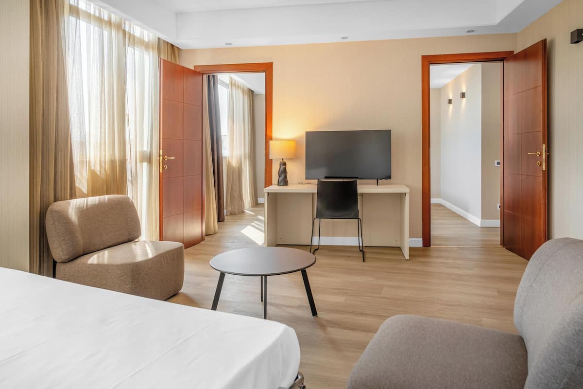 Ein Hotelzimmer mit einem Bett, einem Schreibtisch mit Fernseher, zwei Sesseln und einem kleinen Tisch.
