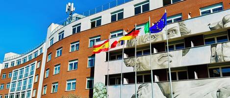Un edificio con varias banderas, incluyendo la bandera de la UE, y una gran escultura de la cabeza de un león.