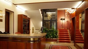 A hotel lobby with a reception desk, a staircase, and a large window with a logo. - Hotel Residence (Parma)