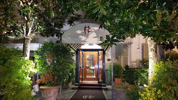 A hotel entrance with a wooden door, a black mat with a symbol, and potted plants on either side. - Hotel Residence (Parma)