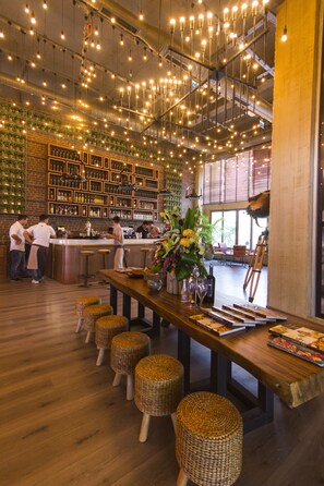 A restaurant interior with a bar area, wooden tables, wicker stools, hanging lights, and a brick wall with shelves of bottles. - DoubleTree by Hilton Bodrum Marina Vista (Bodrum)
