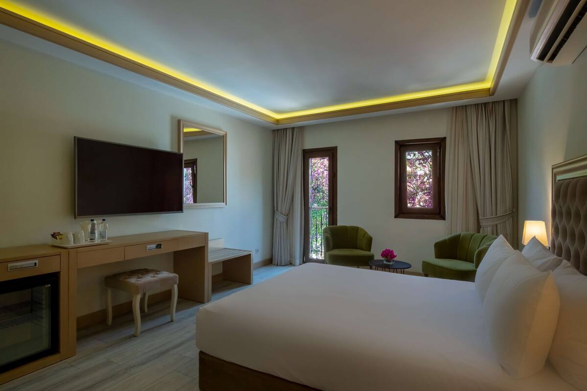 Habitación de hotel con una cama grande, un escritorio, una silla, un televisor y una ventana con cortinas.