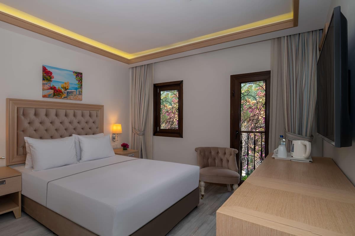 Habitación de hotel con una cama grande, lámparas de noche, un escritorio, una silla y un cuadro en la pared.