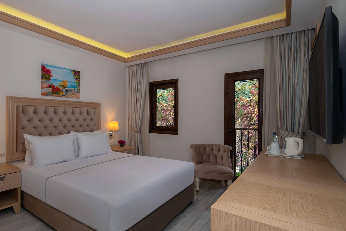 A hotel room with a large bed, bedside lamps, a desk, a chair, and a painting on the wall.