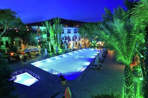 A swimming pool area with lounge chairs and umbrellas, surrounded by trees and buildings. - DoubleTree by Hilton Bodrum Marina Vista (Bodrum)