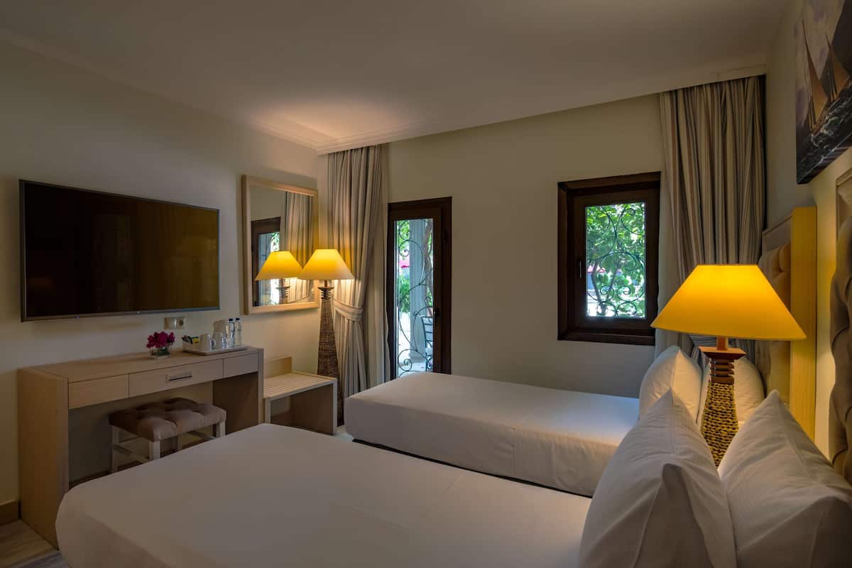 Habitación de hotel con dos camas, un escritorio, un televisor y una ventana con cortinas.