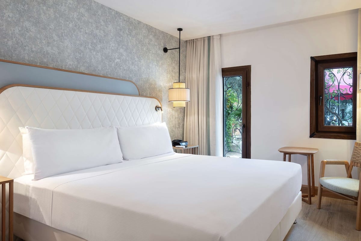 Una habitación de hotel con una cama grande, televisión, una silla y una mesita.