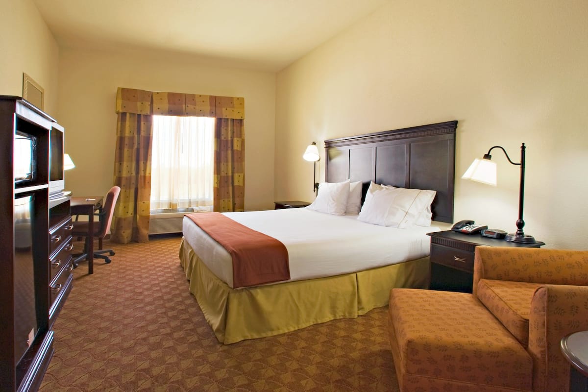 A hotel room with a large bed, a desk, a chair, a TV, and a lamp.