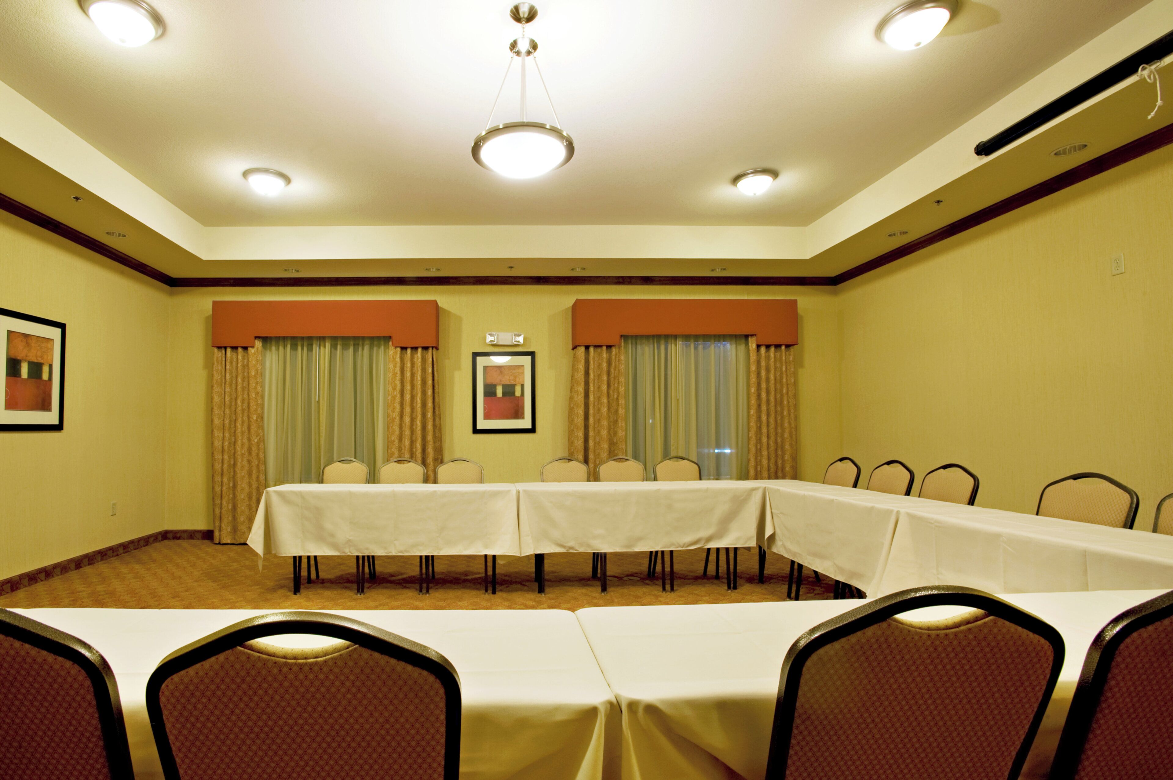 Une salle de conférence avec une longue table, des chaises et des rideaux.