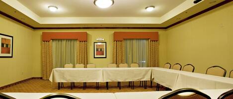 Una sala de conferencias con una larga mesa, sillas y cortinas.