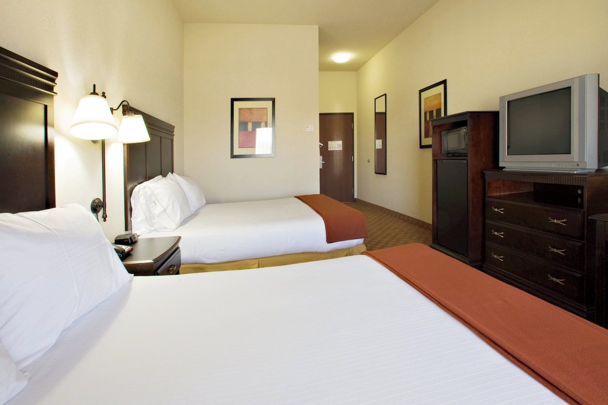 Quarto de hotel com duas camas, televisão, cômoda e porta.