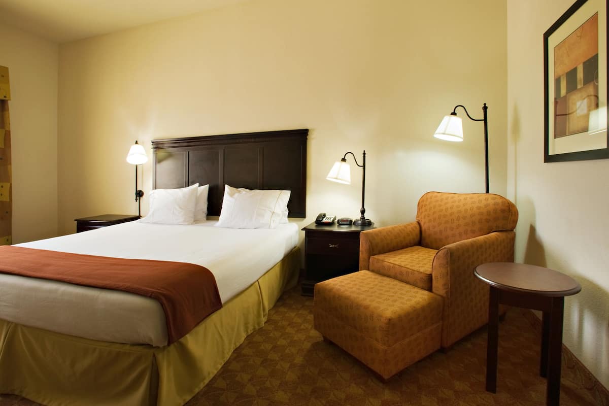 A hotel room with a large bed, two bedside tables, a chair, a small table, and two floor lamps.