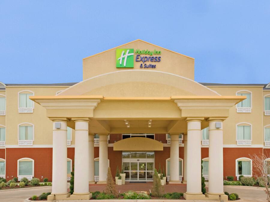Edifício Holiday Inn Express & Suites com entrada central, colunas e céu claro.