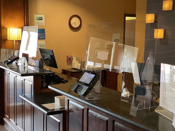 Bancada de recepção de hotel com vários monitores de computador, um relógio e um alarme de incêndio.