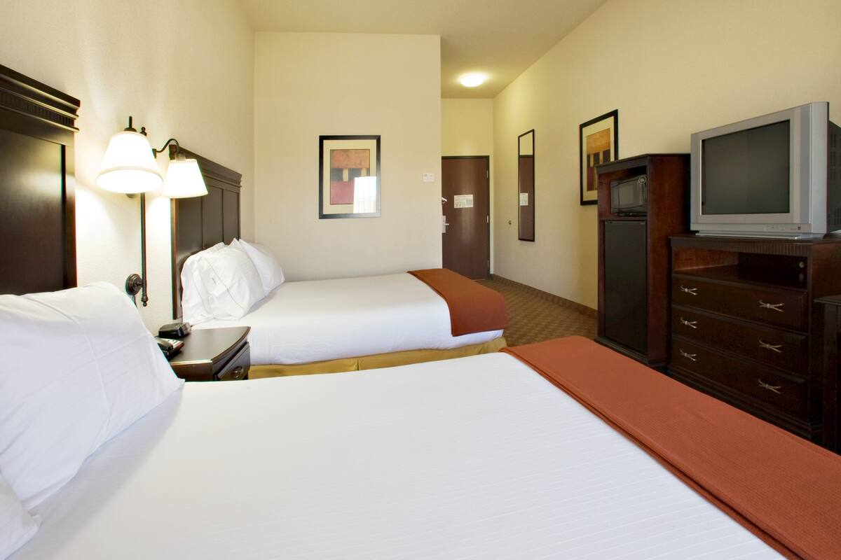 A hotel room with two beds, a television, a dresser, and a door leading to another room.