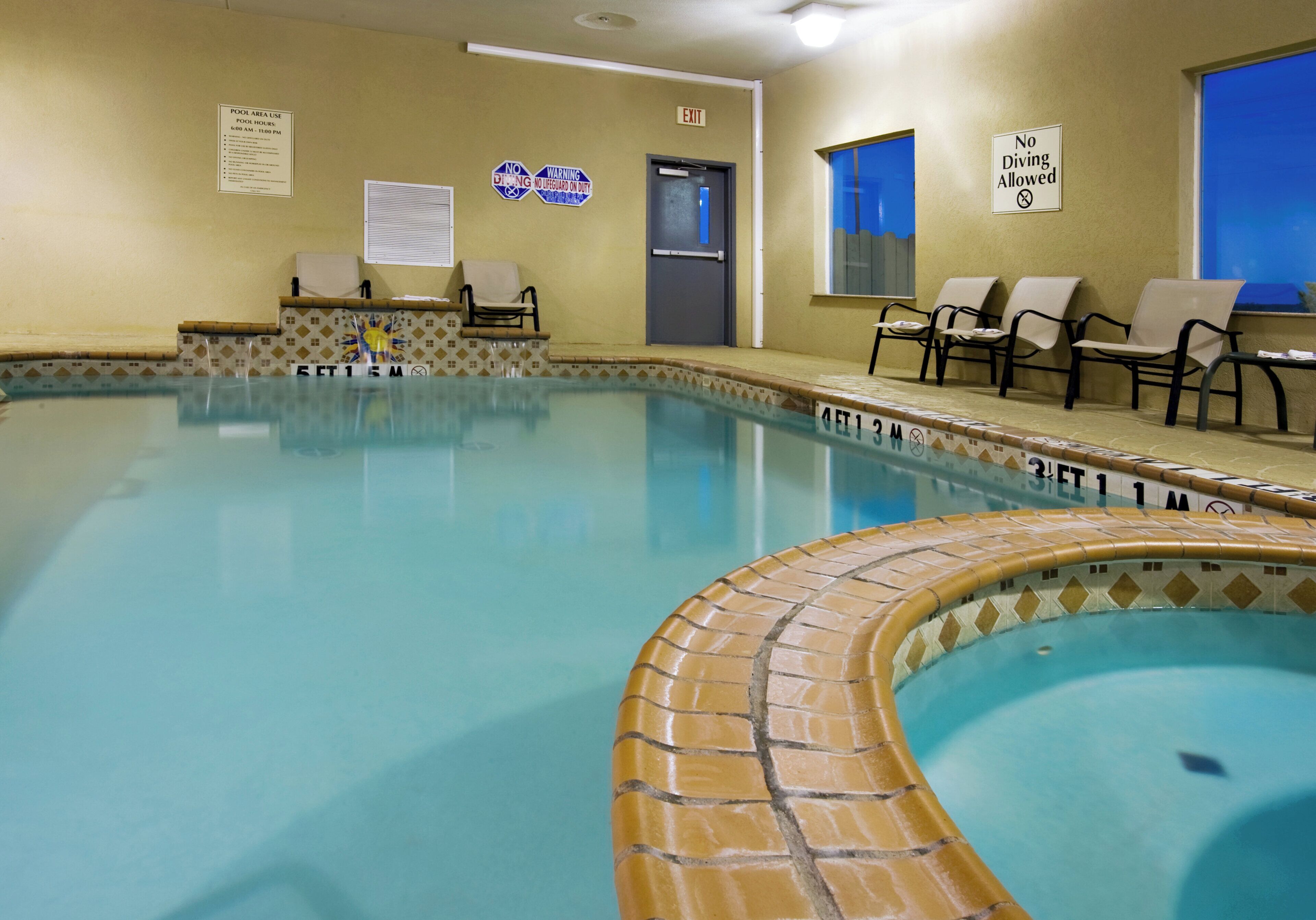 A swimming pool with a tiled edge, lounge chairs, and safety signs on the walls.