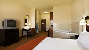 Habitación de hotel con cama, escritorio con silla, televisor, baño con bañera y espejo.