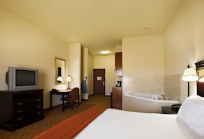 Quarto de hotel com cama, escrivaninha com cadeira, televisão, banheiro com banheira e espelho.