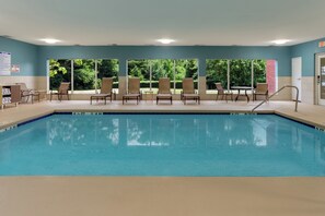 A swimming pool with lounge chairs and a table, surrounded by windows with a view of greenery. - Holiday Inn Express Hotel & Suites Charlotte Arrowood by IHG (Charlotte)