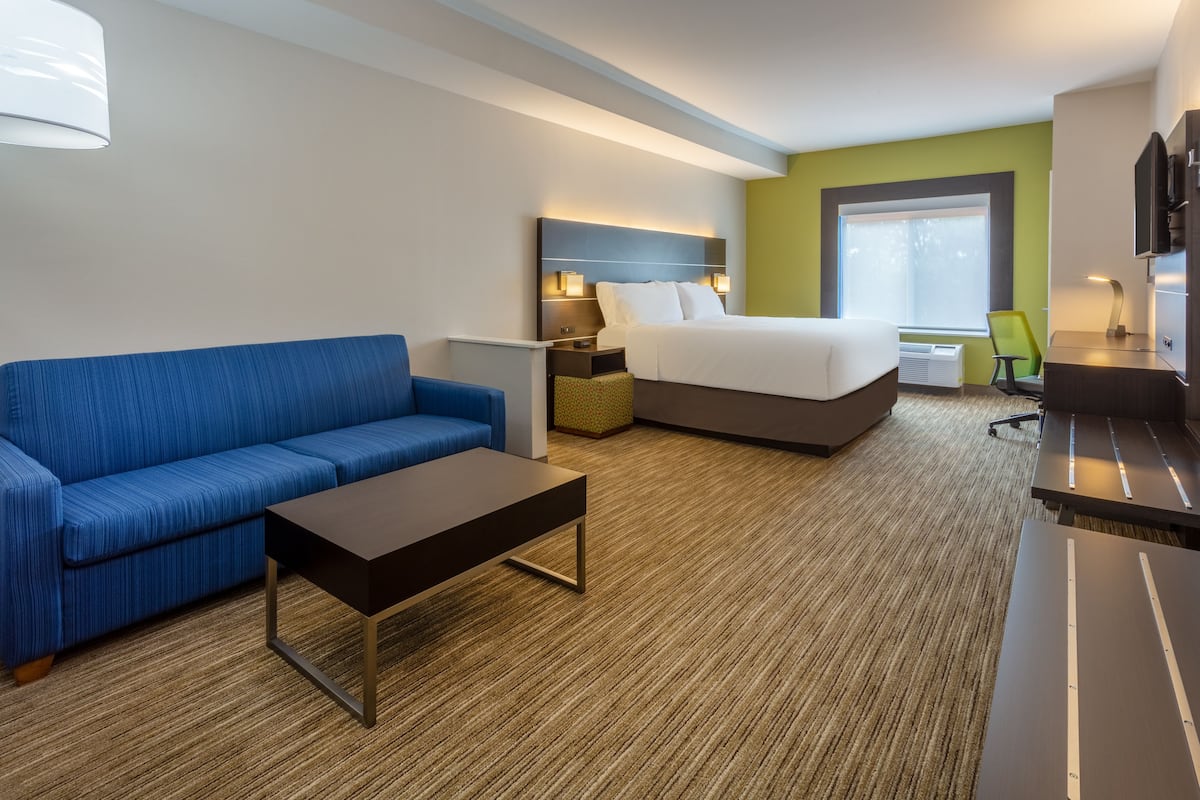 A hotel room with a blue sofa, a bed, a desk, and a TV.