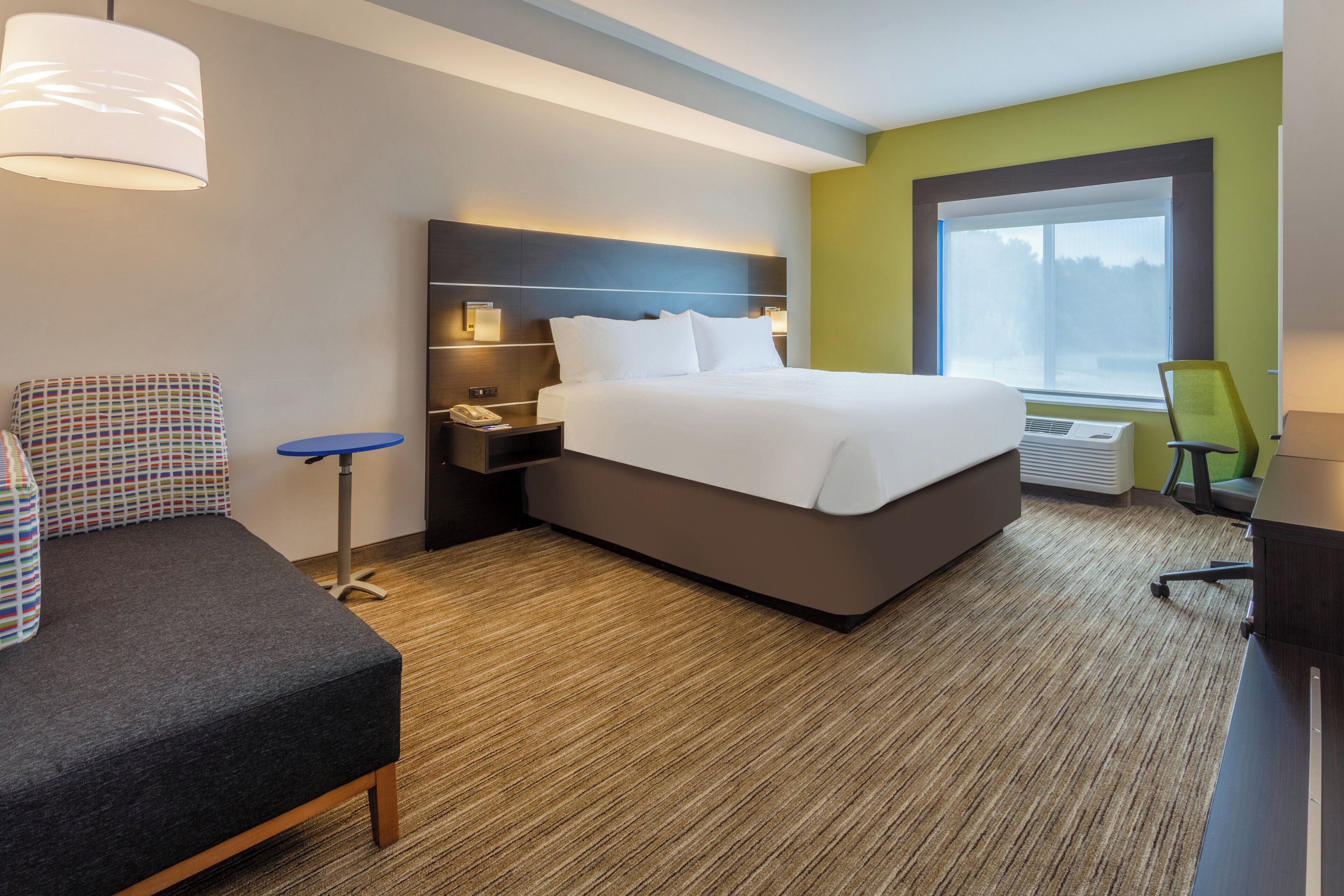 Une chambre d’hôtel avec un lit, une table de chevet, une lampe, une chaise et une fenêtre donnant sur un paysage agréable.