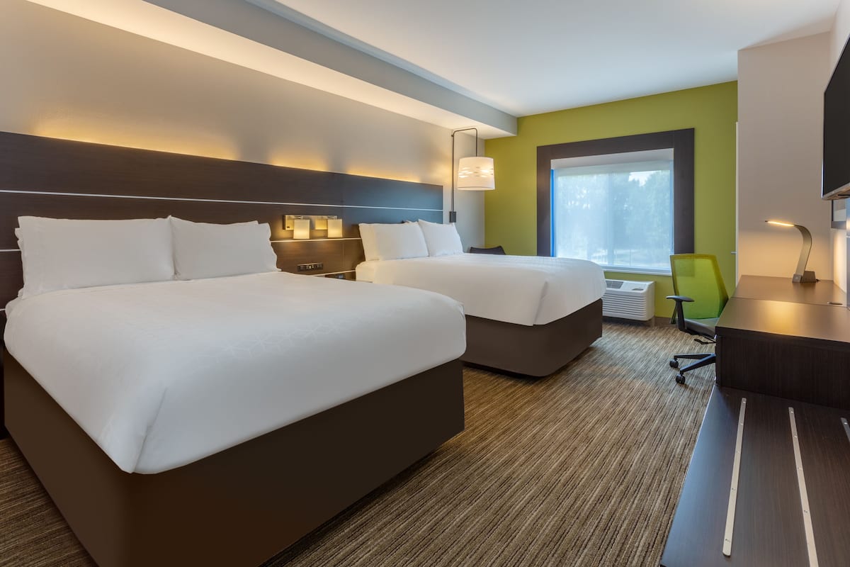 A hotel room with two beds, a desk, a chair, and a large window.