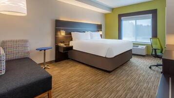 A hotel room with a bed, bedside table, lamp, chair, and a window with a view.