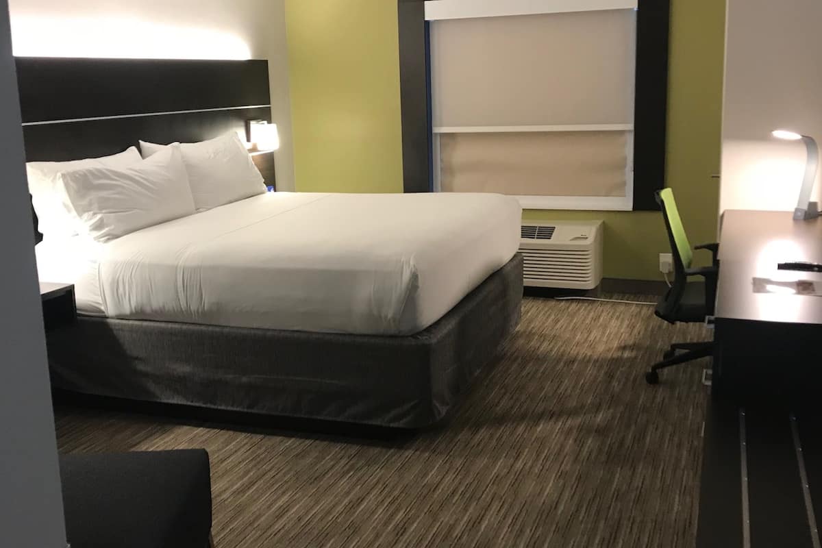 A hotel room with a bed, a desk, a chair, and a window with blinds.