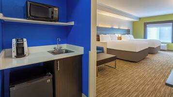 A hotel room with a kitchenette, a bed, a desk, and a window.