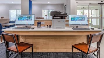 Una mesa de recepción con dos monitores de computadora, una impresora y un área de asientos con sillas.