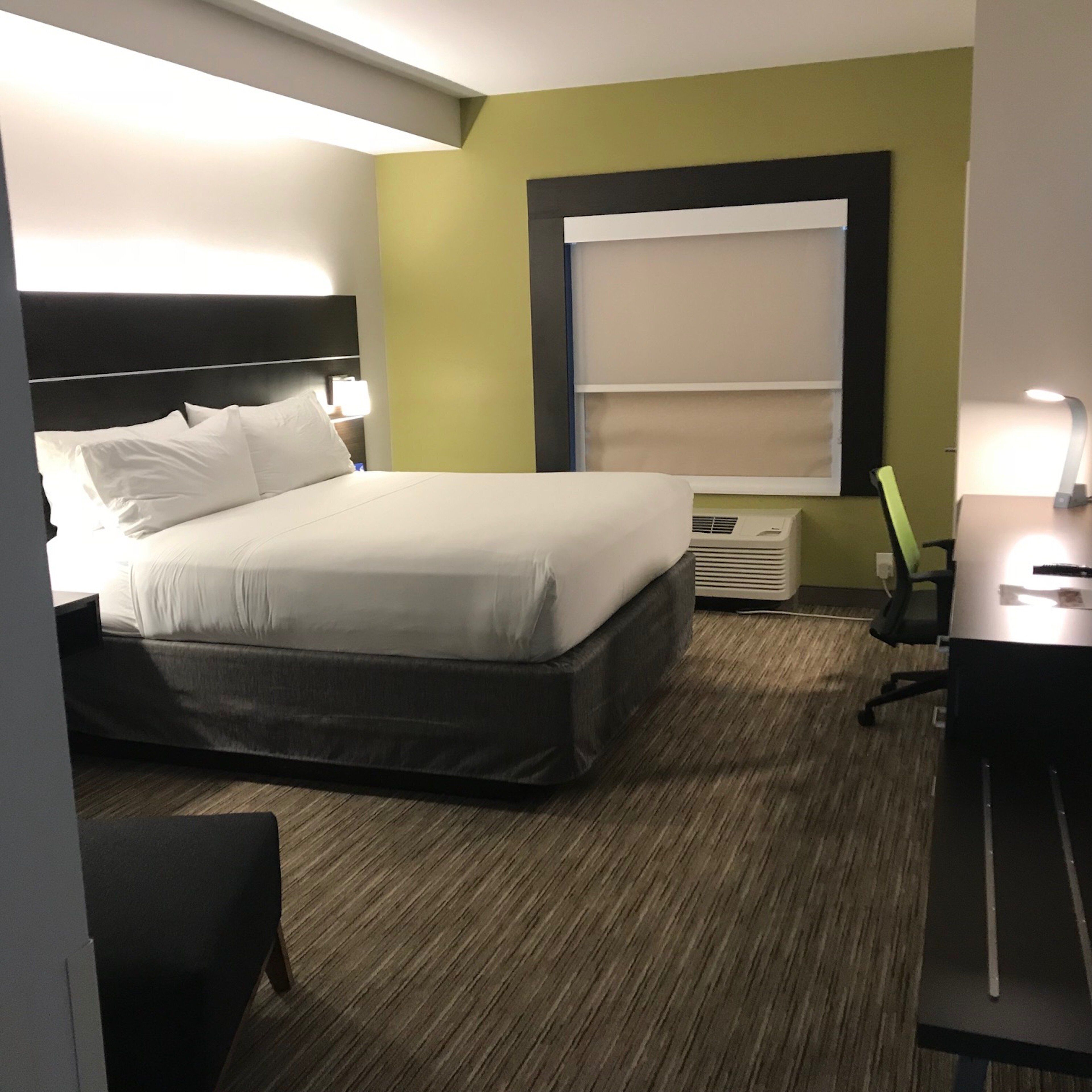 A hotel room with a bed, a desk, a chair, and a window with blinds.