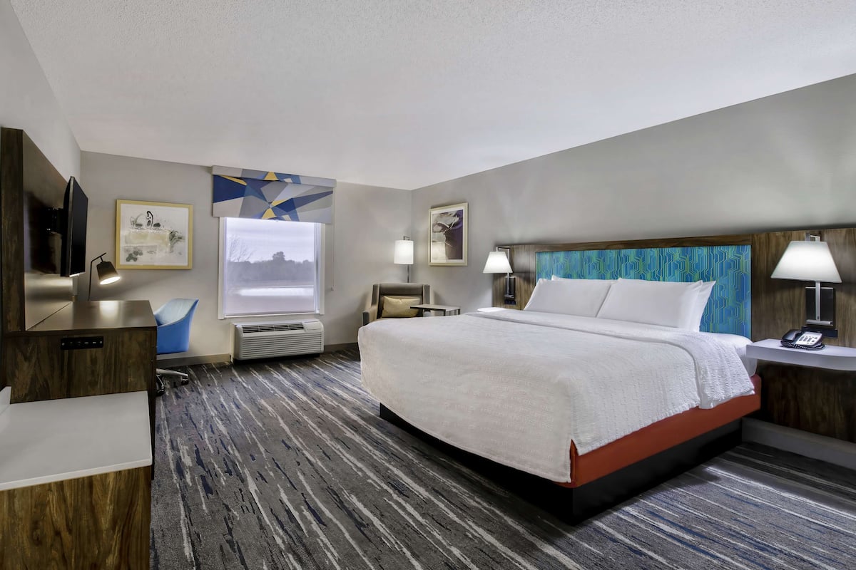 A hotel room with a large bed, a desk, a chair, a TV, and artwork on the walls.