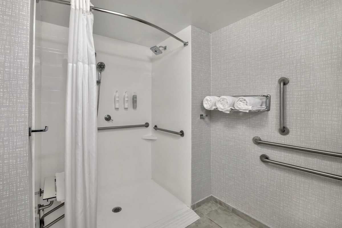 A modern bathroom with a walk-in shower, grab bars, and a towel rack.