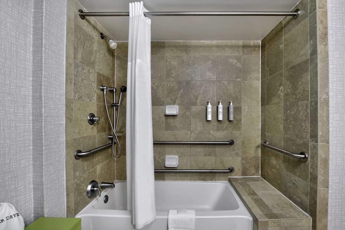 A modern bathroom with a bathtub, shower, and grab bars.