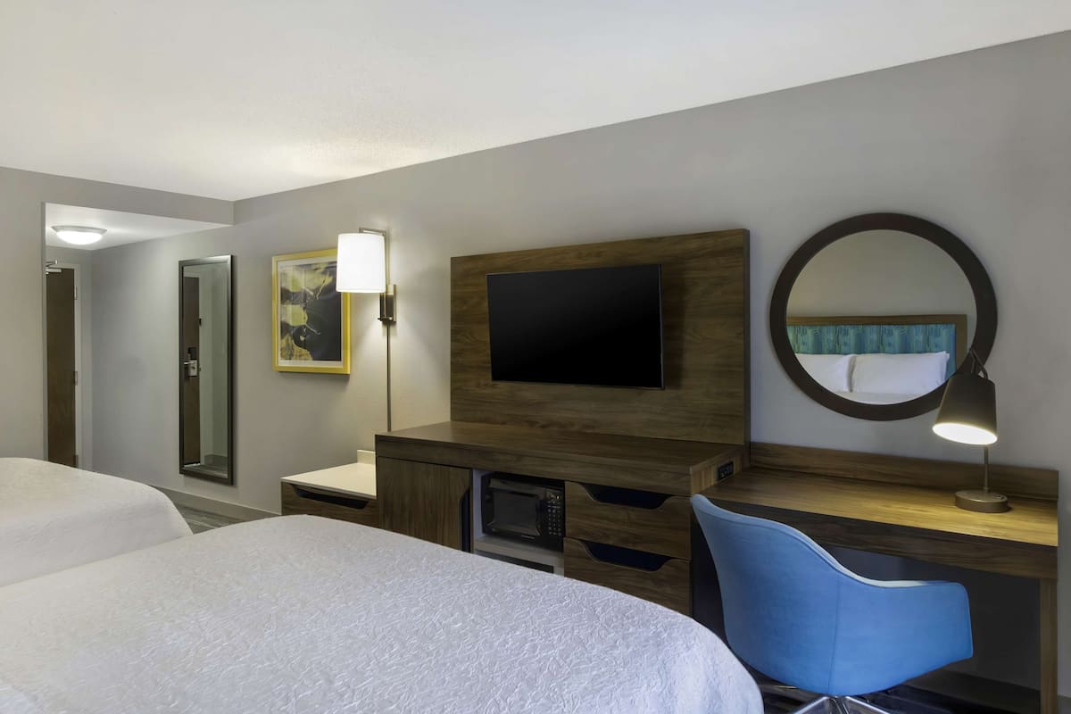A hotel room with two beds, a TV, a mirror, a desk with a lamp, and a microwave.