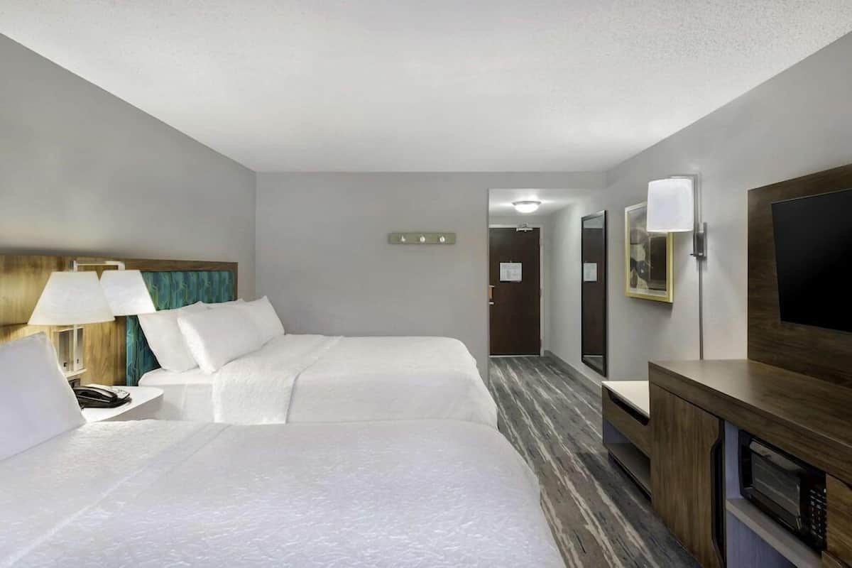 A hotel room with two beds, a desk with a lamp, a TV, and a microwave.