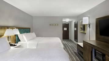 A hotel room with two beds, a desk with a lamp, a TV, a microwave, and a door leading to another room.