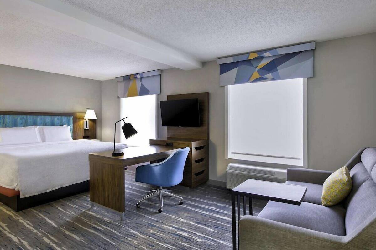 A hotel room with a bed, desk, chair, TV, and sofa.