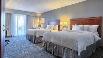 A hotel room with two beds, a large window with curtains, a desk, and a chair.