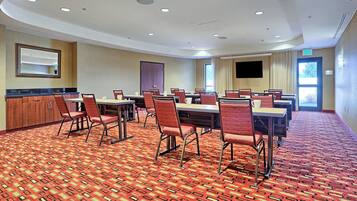 Sala de conferências com carpete estampado, várias mesas e cadeiras.