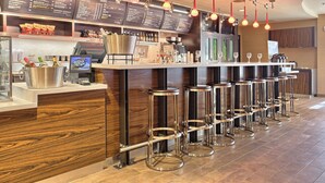 A bar area with a menu board, bar stools, and a counter with a cash register and bottles. - Courtyard by Marriott Harrisburg West/Mechanicsburg (Mechanicsburg)