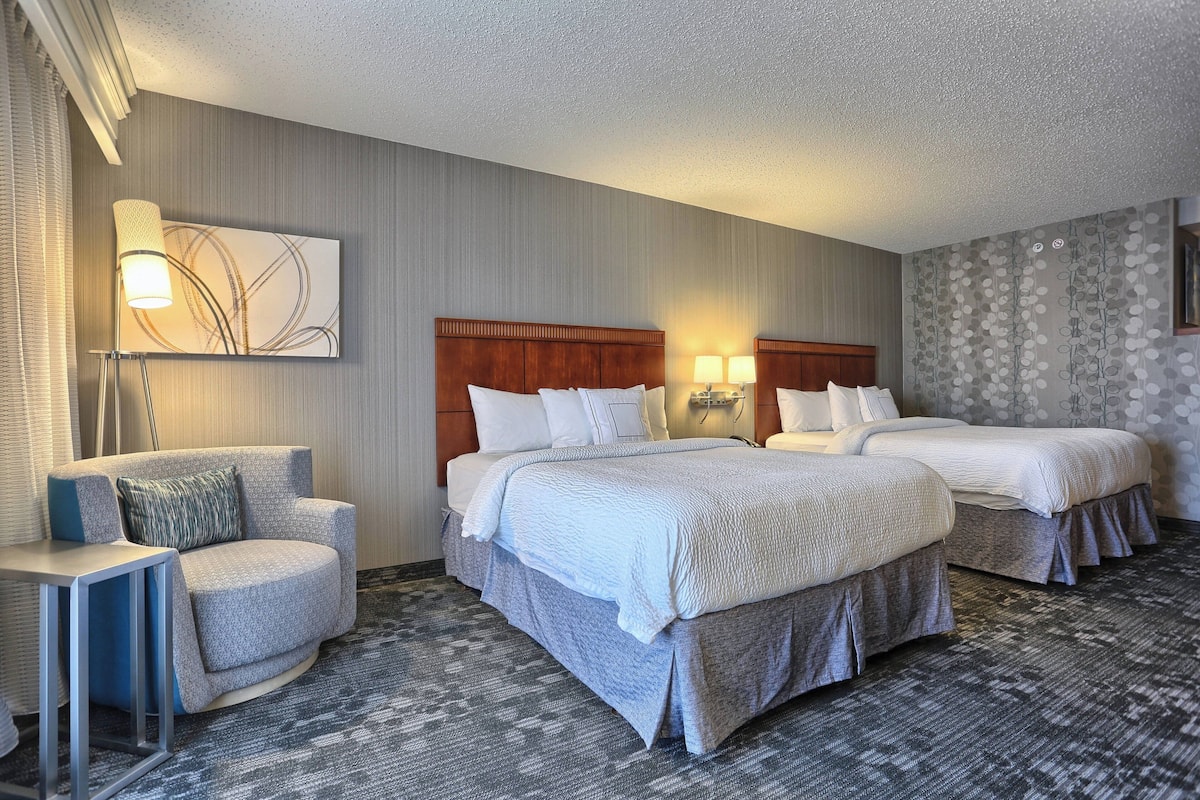 Une chambre d’hôtel avec deux lits, un canapé, une table d’appoint et une lampe fixée au mur.