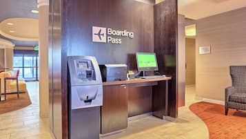 Ett modernt incheckningsområde med en skylt som visar ”Boarding Pass”, en bankomat och en datorskärm.
