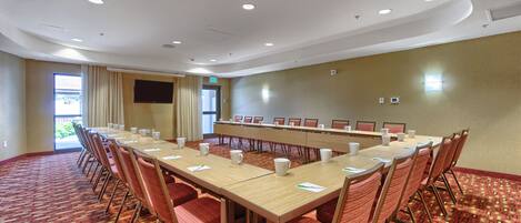 A conference room with a long table, red chairs, and a carpeted floor.