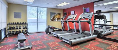A gym with treadmills, an elliptical, dumbbells, and a bench.