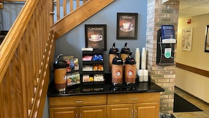 A coffee station with espresso and cappuccino options, a trash bin, and a safety sign.