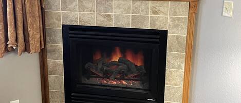 Una chimenea con detalles de azulejos, una planta en maceta encima y una cortina a la izquierda.