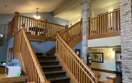 A multi-level wooden staircase with a chandelier, a brick column, and a coffee machine on the lower level.